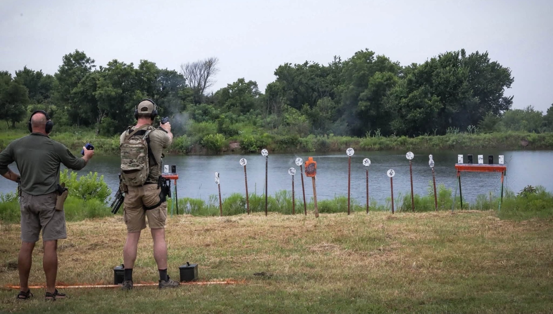 Competitor engaging a steel plate rack across the pond on a summer Run N Gun stage at The Burial Mound