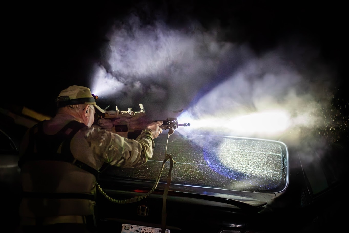 White-light shooter engaging targets across a vehicle hood during the Twilight Biathlon night stage