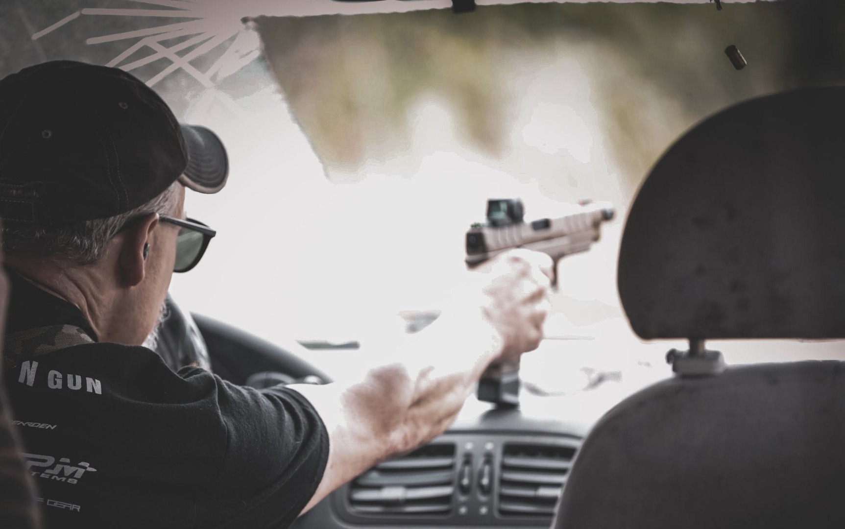 Competitor engaging targets with a pistol through a vehicle windshield on a Run N Gun stage at The Burial Mound